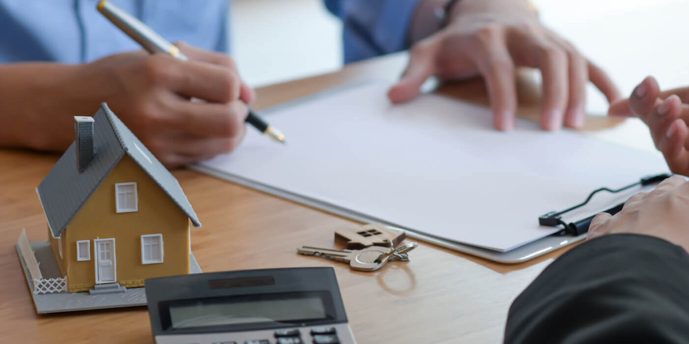 Two people at a table with a calculator and a house model.