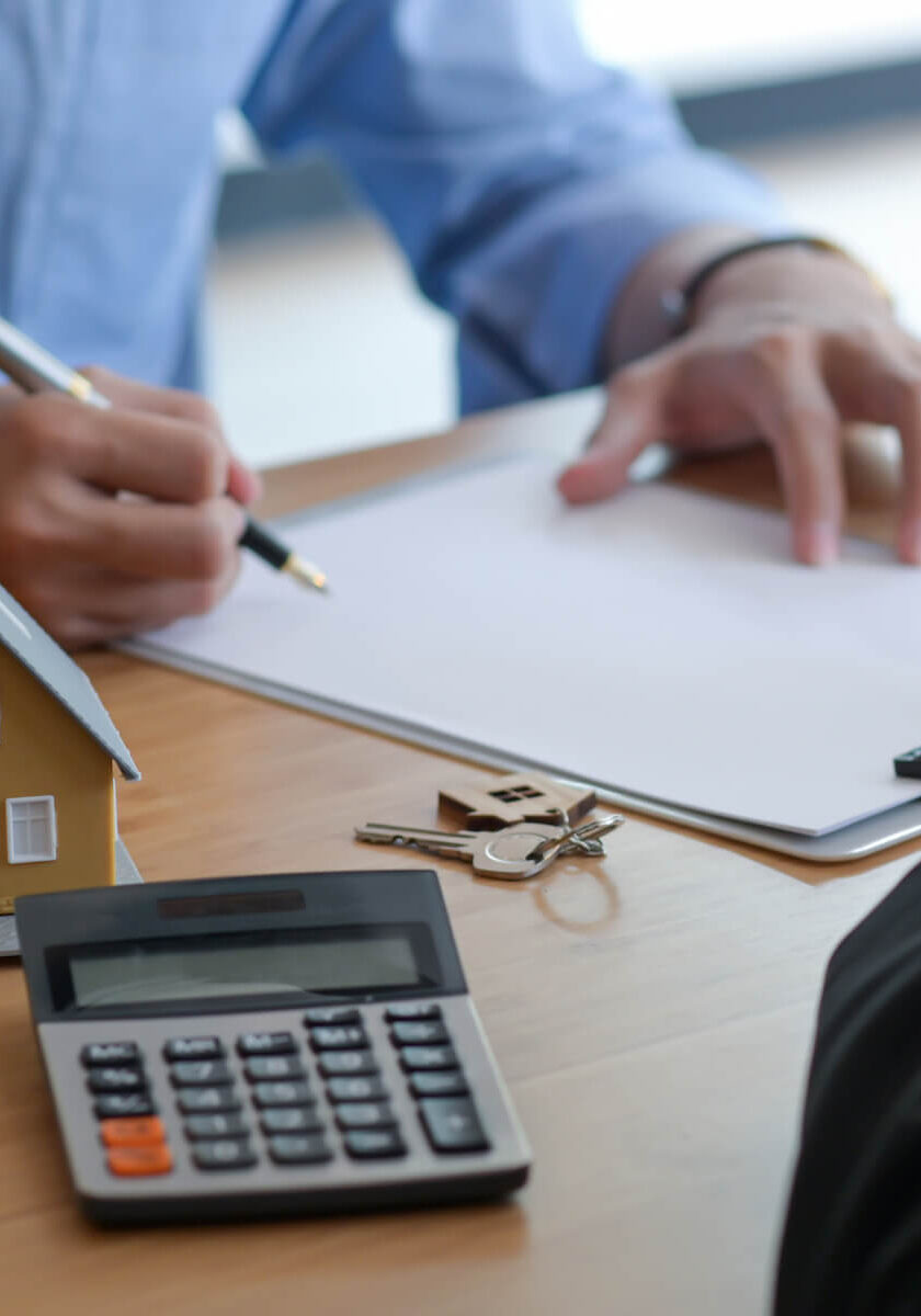 Two people at a table with a calculator and a house model.